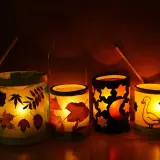 Vier selbstgebastelte Tischlaternen für Kinder leuchten warm. Mit Blättern, Sternen, Mond und einem Gänse-Motiv.