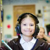 Ein lächelndes Mädchen mit Kopfhörern im Klassenzimmer. Möglicherweise ein Hinweis auf ADHS-Symptome bei Kindern, die sich in Konzentrationsschwierigkeiten äußern.