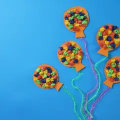 Bunte Ballons aus Papier, ideal zum Fasching Deko basteln. Kleine, zerknüllte Papierstücke in Rot, Blau, Grün und Gelb zieren die orangefarbenen Ballons.