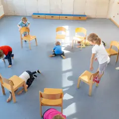 Kinder spielen in der Turnhalle, nutzen Stühle für kreative Ideen und Bewegung.