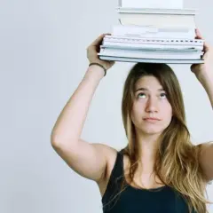 Junge Frau balanciert Bücher auf dem Kopf. Das Gewicht symbolisiert den Lernaufwand im Gymnasium und die Herausforderung des strukturierten Lernens.