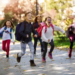 Fröhliche Grundschüler mit Rucksäcken rennen auf dem Schulweg nach den Ferien.