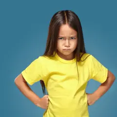 Ein kleines Mädchen mit ernstem Gesichtsausdruck und Händen in den Hüften, das aggressives Verhalten bei Kindern im Kindergarten zeigt.
