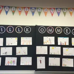 Willkommen zur 1. Klasse! Kinderzeichnungen schmücken die Tafel, ein bunter ABC-Girlande hängt darüber.