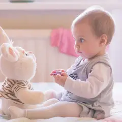 Ein Baby spielt mit einem Stoffhasen. Die Augen des Babys sind auf den Hasen gerichtet, was auf frühe Anzeichen von Autismus hindeuten könnte.