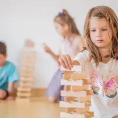 Kinder gestalten eine Bauecke im Kindergarten. Ein Mädchen baut konzentriert einen Turm aus Holzklötzen.