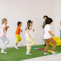 Kindergartenkinder rennen fröhlich über den grünen Teppich, als ob sie Tiere wären. Die Erzieherinnen machen mit bei den lustigen Bewegungsspielen.
