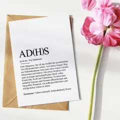 ADHS-Diagnostik online: Ein Blatt mit der Definition von ADHS liegt auf einem Umschlag, daneben eine rosa Blüte.