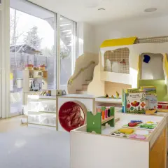 Ein heller, freundlicher gruppenraum raumgestaltung kita ideen mit Spielturm, Rutsche, Spielküche und vielen Spielsachen.