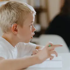 Junge mit Hörgerät, der auf ein Buch zeigt. Mögliche ADHS-Ursachen werden diskutiert, während er sich konzentriert.