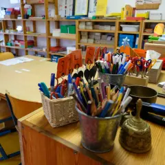 Buntstifte, Scheren und ein Gong auf einem Tisch in einer Montessori-Schule. Die Kosten für eine Montessori-Schule können variieren.