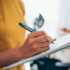 Person schreibt auf einem Klemmbrett. Wenn Sie sich fragen, wie finde ich heraus ob ich ADHS habe, könnte dies der erste Schritt sein: Notizen machen.