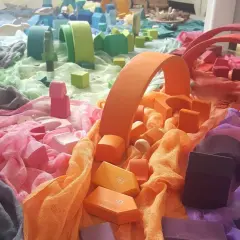 Bunte Stoffe und Holzbausteine, die an eine Regenbogenstadt erinnern. Perfekt für einen kreativen Kindergartenbericht schreiben.