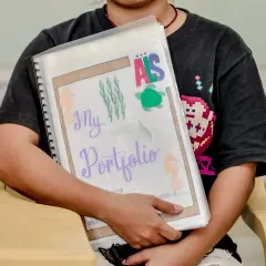 Ein Kind hält stolz sein **Portfolio Kindergarten** mit maritimen Motiven. Seepferdchen, Quallen und eine Schildkröte zieren die Mappe.