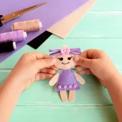 Kleine Hände basteln eine Filzpuppe. Schere, Faden und Filz liegen bereit für das Filzen mit Kindern.