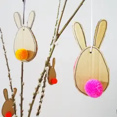 Osterhasen aus Pappe mit bunten Bommeln als Schwänzen, perfekt zum Basteln Ostern Kinder. Hängen an Weidenkätzchen-Zweigen.