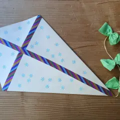 Ein selbstgebastelter Drachen aus Tonpapier mit Schneeflocken und bunten Bändern. Die Schnur hat kleine grüne Schleifen und Holzperlen.