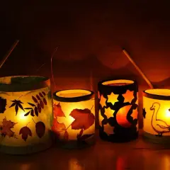 Vier selbstgebastelte Tischlaternen für Kinder leuchten warm. Mit Blättern, Sternen, Mond und einem Gänse-Motiv.