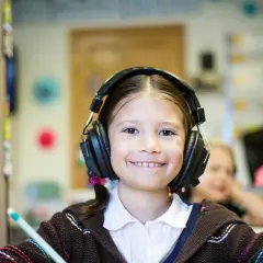 Ein lächelndes Mädchen mit Kopfhörern im Klassenzimmer. Möglicherweise ein Hinweis auf ADHS-Symptome bei Kindern, die sich in Konzentrationsschwierigkeiten äußern.