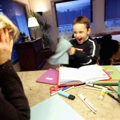 Ein Junge mit ADHS wirft Papier, während seine Mutter verzweifelt die Hände vors Gesicht schlägt.