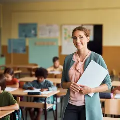 Lehrerberuf pro contra: Eine lächelnde Lehrerin mit Unterlagen steht vor einer Klasse voller konzentrierter Schüler.