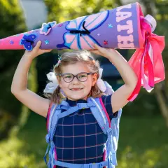 Ein Mädchen mit Schultüte und Rucksack, bereit für die erste Klasse Grundschule. Bunte Schmetterlinge zieren die Schultüte.