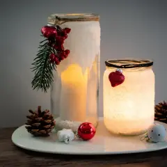 Zwei selbstgebastelte Windlichter mit Salz, Kerzen und weihnachtlichem Schmuck. Ein DIY-Projekt, das Gemütlichkeit bringt.