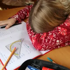 Müdes Kind mit Kopf auf dem Schreibtisch, umgeben von Schulbüchern und Stiften. Vielleicht helfen Ritalin Tabletten bei der Konzentration?