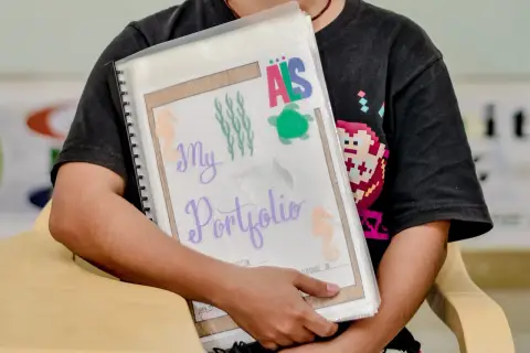 Ein Kind hält stolz sein **Portfolio Kindergarten** mit maritimen Motiven. Seepferdchen, Quallen und eine Schildkröte zieren die Mappe.
