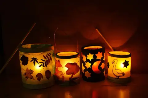 Vier selbstgebastelte Tischlaternen für Kinder leuchten warm. Mit Blättern, Sternen, Mond und einem Gänse-Motiv.