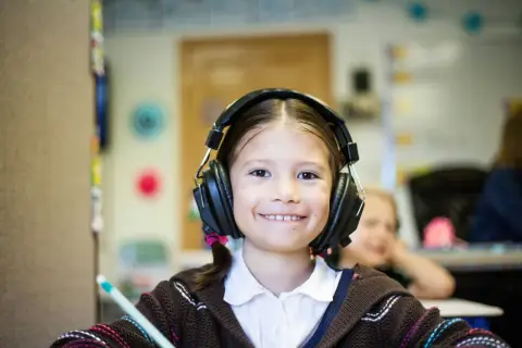 Ein lächelndes Mädchen mit Kopfhörern im Klassenzimmer. Möglicherweise ein Hinweis auf ADHS-Symptome bei Kindern, die sich in Konzentrationsschwierigkeiten äußern.