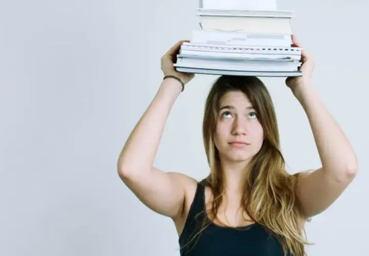Junge Frau balanciert Bücher auf dem Kopf. Das Gewicht symbolisiert den Lernaufwand im Gymnasium und die Herausforderung des strukturierten Lernens.