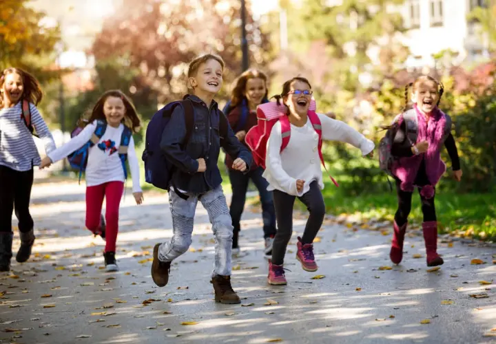 Fröhliche Grundschüler mit Rucksäcken rennen auf dem Schulweg nach den Ferien.