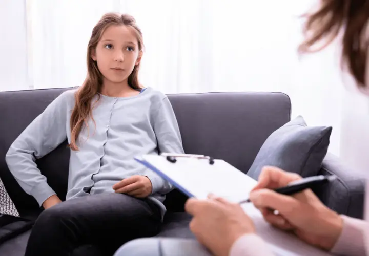 Ein Mädchen sitzt auf einer Couch und spricht mit einer Person, die Notizen macht. Die Frage, ob ADHS heilbar ist, wird hier thematisiert.