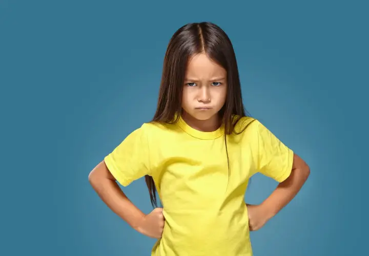Ein kleines Mädchen mit ernstem Gesichtsausdruck und Händen in den Hüften, das aggressives Verhalten bei Kindern im Kindergarten zeigt.