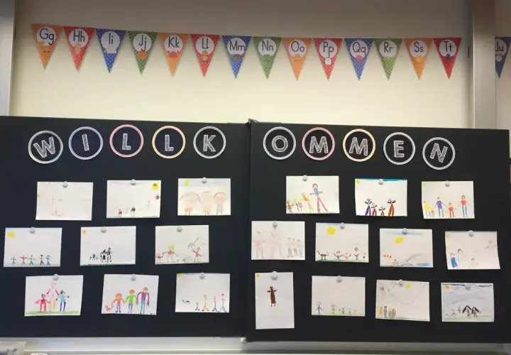 Willkommen zur 1. Klasse! Kinderzeichnungen schmücken die Tafel, ein bunter ABC-Girlande hängt darüber.