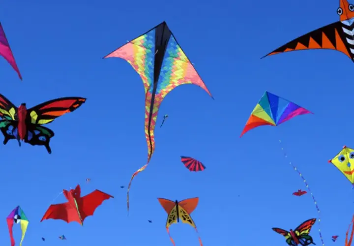 Bunte Drachen in Form von Schmetterlingen, Fledermäusen und geometrischen Mustern steigen im blauen Himmel auf. Ein Fest des Drachenbastelns!
