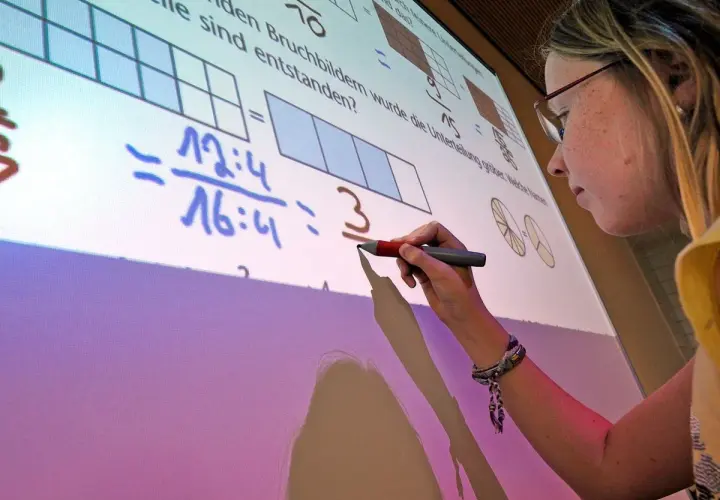 Ein Mädchen schreibt auf einem interaktiven Whiteboard, das Matheaufgaben zeigt. Solche Whiteboards sind moderne Tafeln für den Unterricht.
