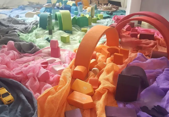 Bunte Stoffe und Holzbausteine, die an eine Regenbogenstadt erinnern. Perfekt für einen kreativen Kindergartenbericht schreiben.
