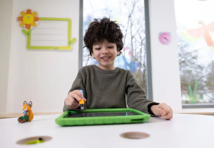 Ein Junge übt mit einem Stift auf einem Tablet, was eine spielerische Art ist, graphomotorische Fähigkeiten zu entwickeln.