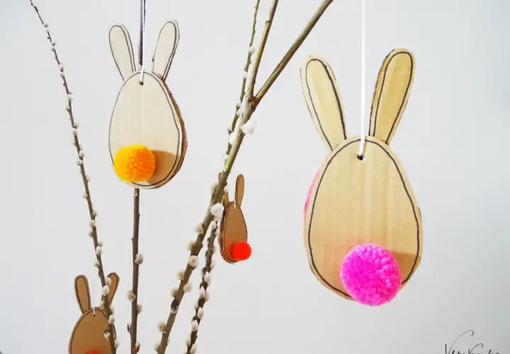 Osterhasen aus Pappe mit bunten Bommeln als Schwänzen, perfekt zum Basteln Ostern Kinder. Hängen an Weidenkätzchen-Zweigen.