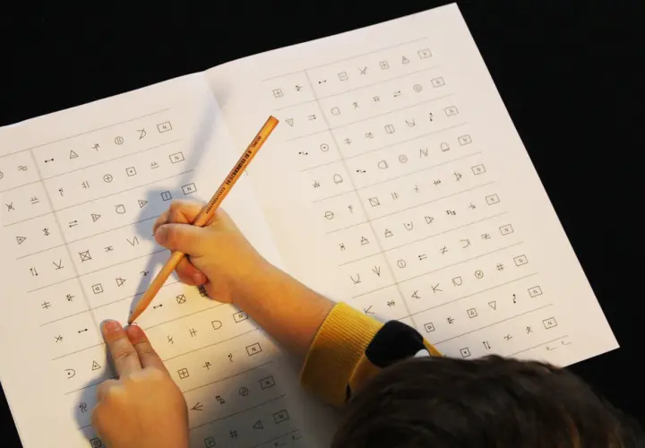 Kind löst einen dyskalkulie test mit Symbolen. Ein Bleistift zeigt auf ein Symbol auf dem Blatt.