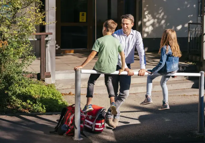 Ein Mann spricht mit zwei Kindern vor einer Schule. Vielleicht plant er, als lehrer bundesland wechseln.