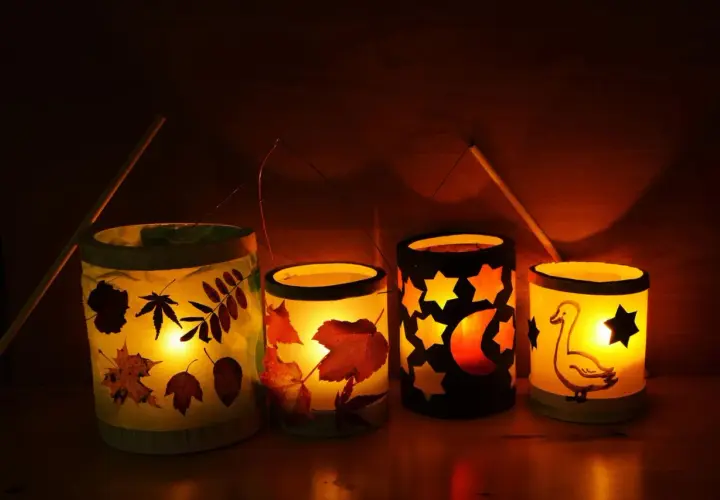 Vier selbstgebastelte Tischlaternen für Kinder leuchten warm. Mit Blättern, Sternen, Mond und einem Gänse-Motiv.
