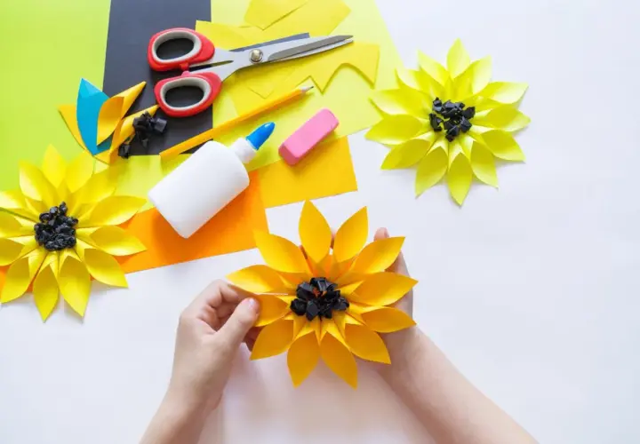 Kinder basteln bunte Papierblumen. Schere, Kleber und Papier liegen bereit für kreative Projekte.