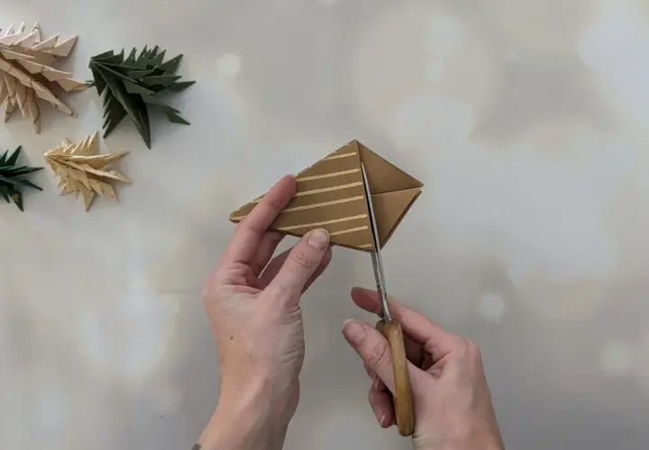 Schere schneidet Papier für einen Tannenbaum. Einfache Anleitung zum Falten von Tannenbäumen.