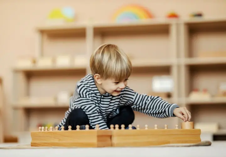 Ein Junge spielt konzentriert mit Holzbausteinen in einem Montessori Kindergarten.