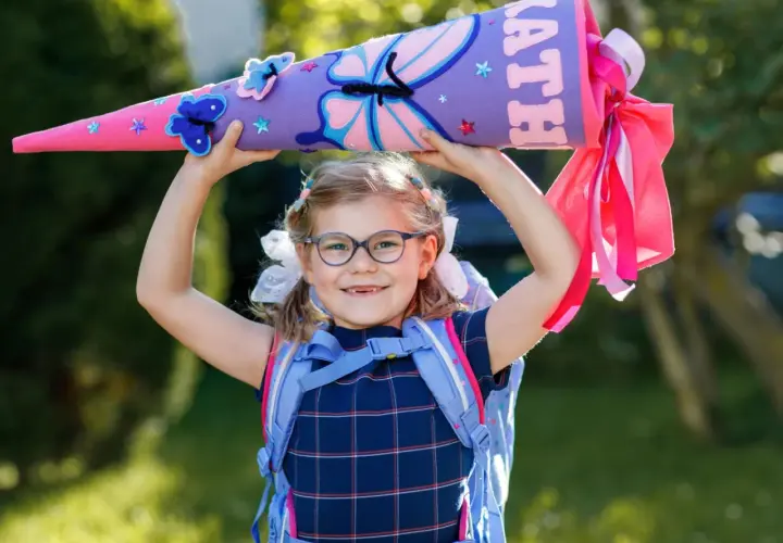 Ein Mädchen mit Schultüte und Rucksack, bereit für die erste Klasse Grundschule. Bunte Schmetterlinge zieren die Schultüte.