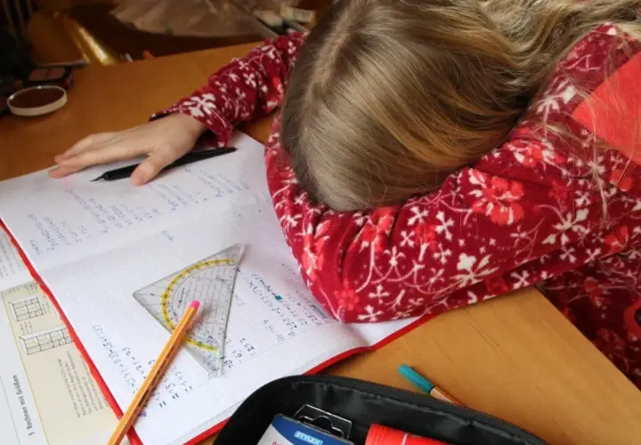 Müdes Kind mit Kopf auf dem Schreibtisch, umgeben von Schulbüchern und Stiften. Vielleicht helfen Ritalin Tabletten bei der Konzentration?