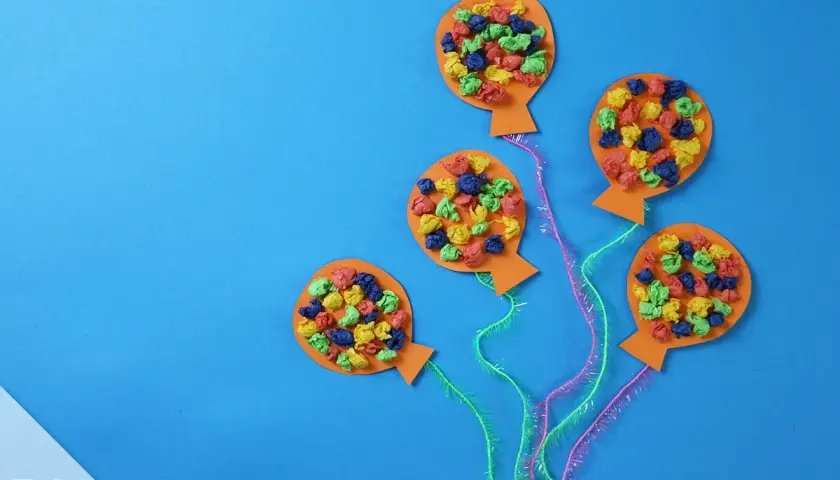 Bunte Ballons aus Papier, ideal zum Fasching Deko basteln. Kleine, zerknüllte Papierstücke in Rot, Blau, Grün und Gelb zieren die orangefarbenen Ballons.